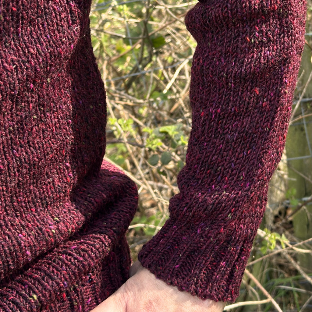 Close-up of a man wearing a dark red speckled knitted garment with a blurred natural background