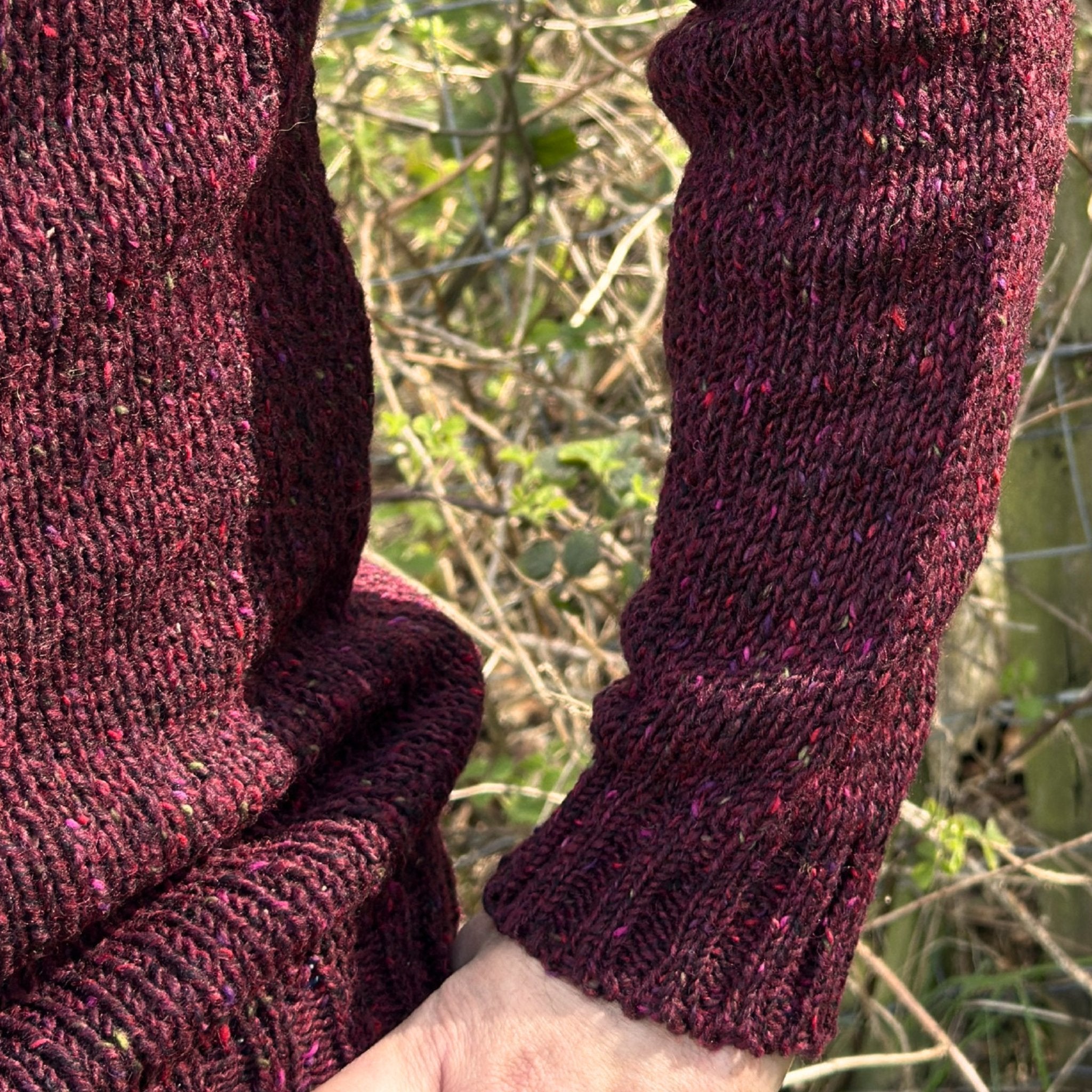 Close-up of a man wearing a dark red speckled knitted garment with a blurred natural background