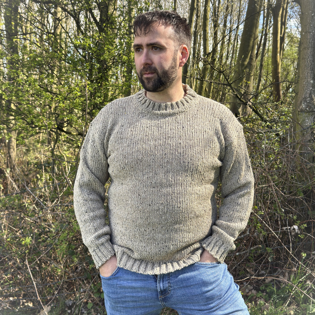 Man wearing a men’s oatmeal crew neck sweater in Donegal wool, handcrafted in Ireland, styled outdoors with blue jeans