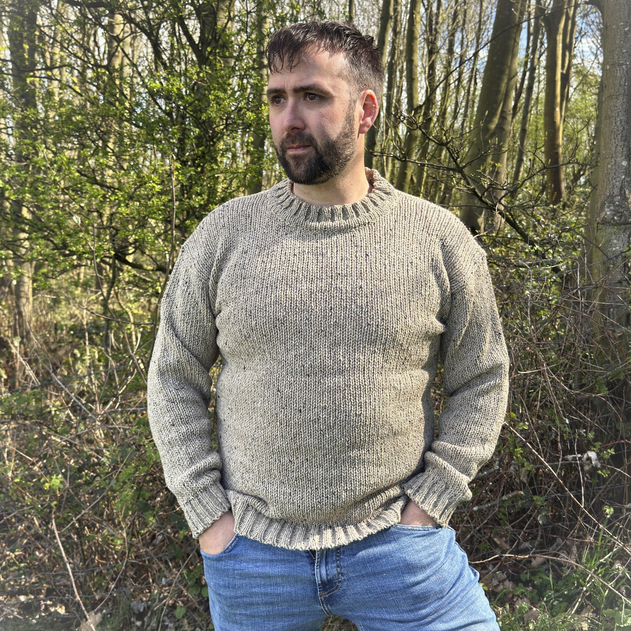 Man wearing a men’s oatmeal crew neck sweater in Donegal wool, handcrafted in Ireland, styled outdoors with blue jeans
