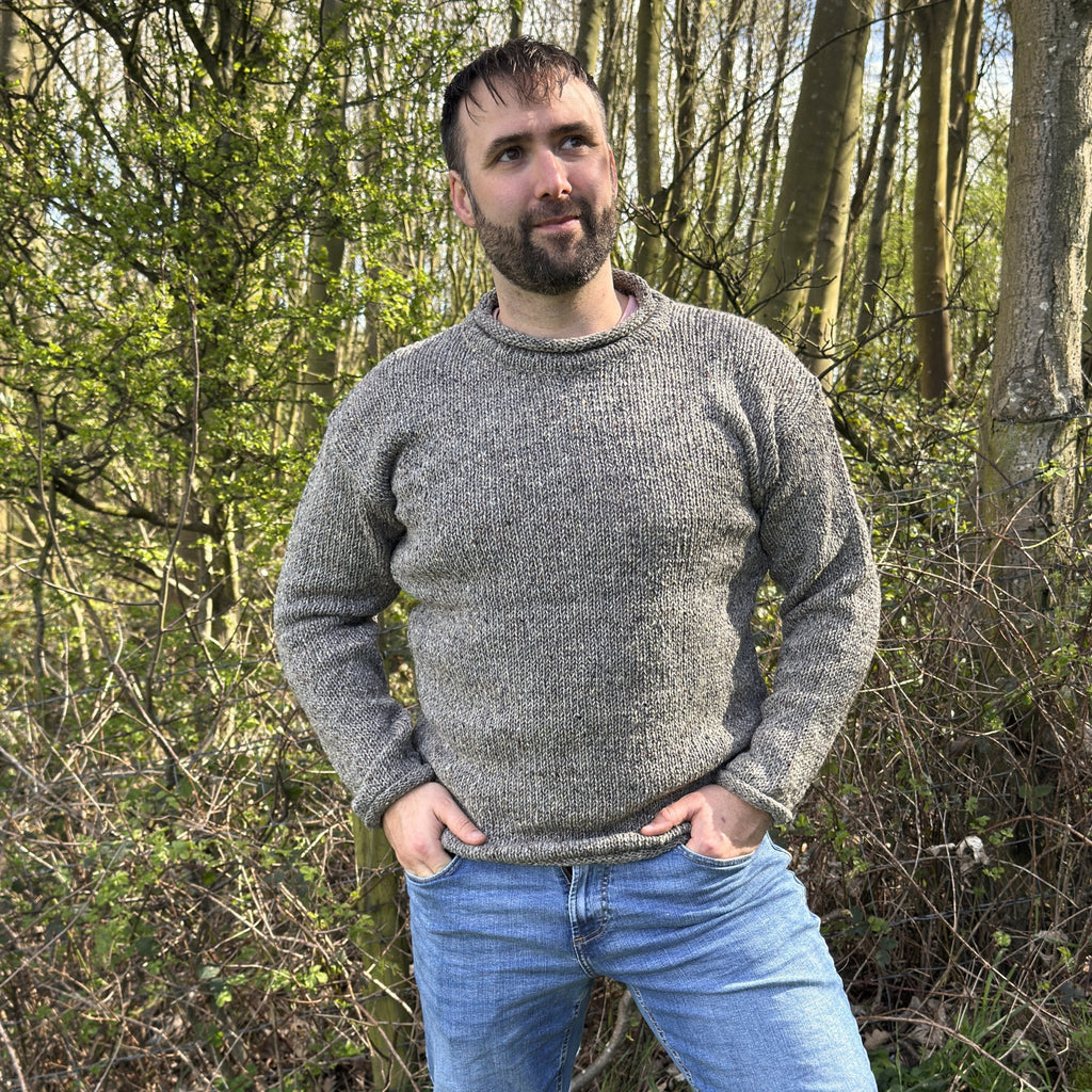 Man wearing a gray sweater and blue jeans standing in a forest.